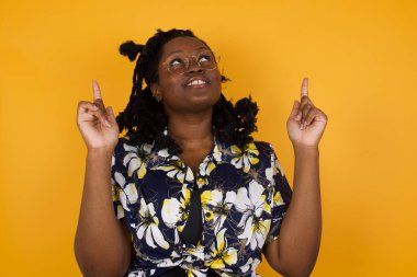  Afro-Amerikan kadın rahat kıyafetler giyip heyecanla haykırıyor, işaret parmaklarını havaya kaldırıyor, boş fotokopi duvarında şok edici bir şey gösteriyor..