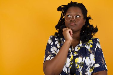 Yüz ifadeleri ve duygular. Düşünceli, genç, güzel, Afro-Amerikan bir kadın. Günlük giysiler giymiş, başının altında el ele tutuşmuş, şüpheli bakışları var..