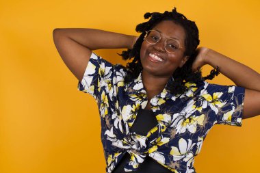 Güven ve cinsel ilişki konsepti. Çekici, Afro-Amerikalı bir kadının portresi. Günlük kıyafetler giymiş, kendinden emin bir ifadeyle gülümseyen ve ellerini başının üstünde tutan bir kadın. Arkaplanda duruyor.