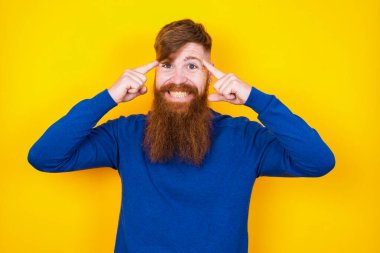 Yakışıklı, kızıl saçlı, beyaz sakallı, sarı duvara karşı duran, ciddi bir bakışla bir fikre konsantre olan, her iki işaret parmağıyla alnını gösteren bir adam..