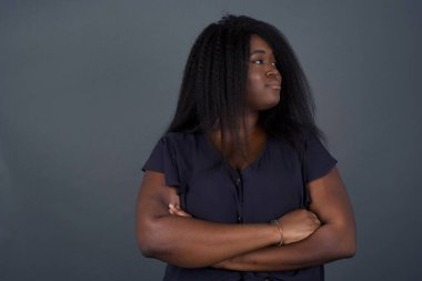 Gri arka planda kollarını kavuşturmuş, üzgün, genç bir Afro-Amerikan kadının görüntüsü. Kötü haberleri dinledikten sonra hayal kırıklığına uğramış bir ifadeyle bakıyorum. Kendine güvenen kız..