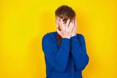 Yakışıklı, kızıl sakallı, beyaz adam sarı duvara karşı duruyor, yüzünü elleriyle kapatıyor ve bir gözü parmaklarının arasında dışarı bakıyor. Bir şeyden ya da birinden korktun mu?.