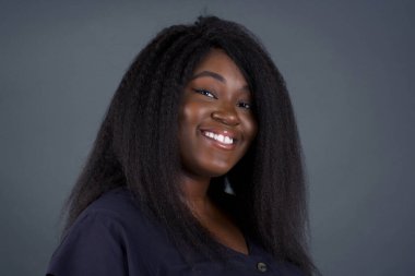 Gri arka planda poz veren güzel Afrikalı Amerikalı kadın gülümsüyor 