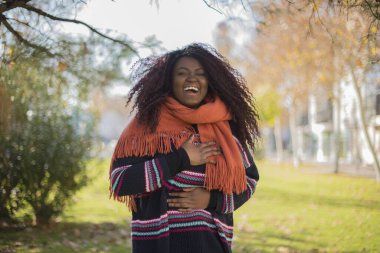 Genç, güzel, gülen Afro-Amerikan kadın sonbahar parkında renkli bir kazak giyiyor.   