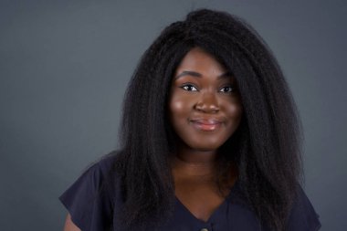 Gri arka planda siyah elbiseli güzel bir Afrikalı kadın.