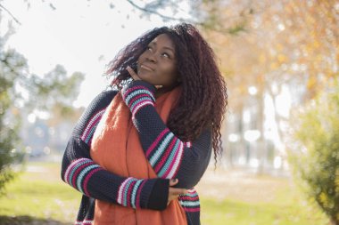 Güz parkında kazak ve eşarp giyen güzel Afro-Amerikan bir kadın.  