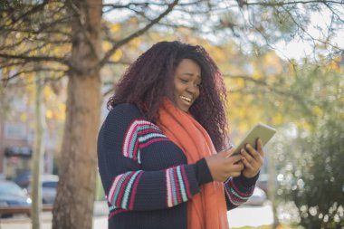 Genç ve güzel Afro-Amerikalı kadın sonbahar parkında kazak ve atkı takıyor.  