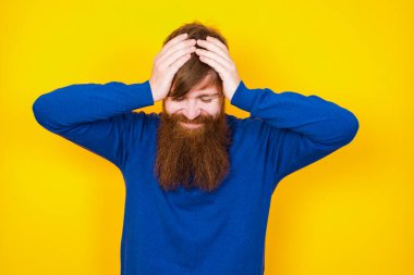 Yakışıklı kızıl saçlı, sakallı beyaz adam sarı duvara karşı duruyor, elleriyle başını tutuyor, şiddetli baş ağrısından muzdarip, şakaklarına parmaklarını bastırıyor.