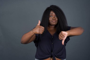 Gri arka planda poz veren genç, dalgın bir Afro-Amerikan kadın iyiye-kötüye işaret veriyor. Sıradan kıyafetler giymekten memnun değil ve etkilenmiyor.