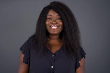 Gri arkaplanda poz veren güzel Afro-Amerikan kadın, gülümsüyor. 