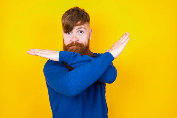 黄色い壁に立っているハンサムな赤毛のひげを被った白人男性は 拒否否否否定的なサインをしている顔と手を交差する怒りの表現を拒否しています — ストック写真