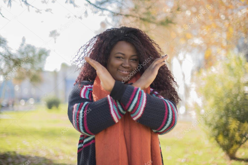 young beautiful  african american woman wearing sweater and orange scarf  gesturing stop  in autumn  park  