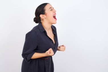 Beyaz stüdyo geçmişine karşı elbise giyen Arap kadın zafere ulaştığına seviniyor ve heyecanlı yumruklar, kapalı gözlerle çığlıklar, başarılı bir insan..