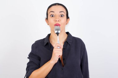 Beyaz stüdyo arka planına karşı giyinmiş güzel, kafası karışık bir Arap kadın stüdyoda kaşıkla bekliyor. 