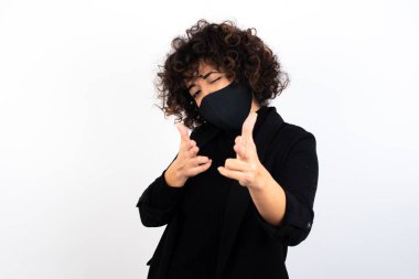 Hey sen, bang. Neşeli ve karizmatik yakışıklı beyaz kadın tıbbi maske takıyor ve parmaklarıyla kameraya mutlu ve küstah bir şekilde işaret ediyor..