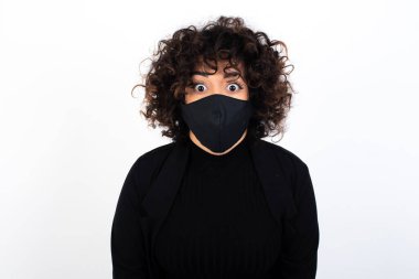 Etkileyici yüz ifadeleri. Şok olmuş beyaz kadın tıbbi maske takıyor, çenesini kapalı tutuyor gördüklerinden sersemlemiş hissediyor..