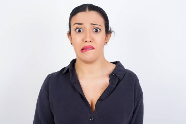 Beyaz stüdyo geçmişine karşı gri elbise giyen genç ve güzel bir Arap kadın gergin ve korkmuş dudakları ısıran sabırsız ifadeli kameraya bakıyor, düşünceli..