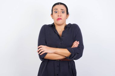 Beyaz stüdyo geçmişine karşı gri elbise giyen genç, güzel bir Arap kadın. Ağzını ısırıyor, endişeli ve korkmuş görünüyor. Kollarını kavuşturuyor, endişe ve şüphe içinde..