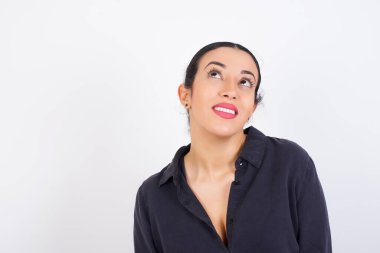 Beyaz stüdyo arka planına karşı gri elbise giyen gizemli genç ve güzel bir Arap kadının portresi gizemli bir gülümsemeyle yukarı bakıyor. Reklam kavramı.