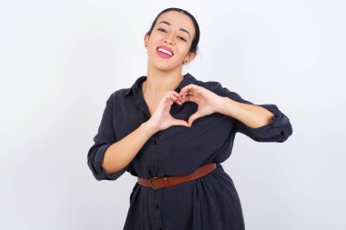 Beyaz stüdyo arka planında giyinmiş Arap bir kadın. Sevgiyle gülümsüyor. Elleriyle kalp sembolü ve şekli gösteriyor. Romantik konsept.