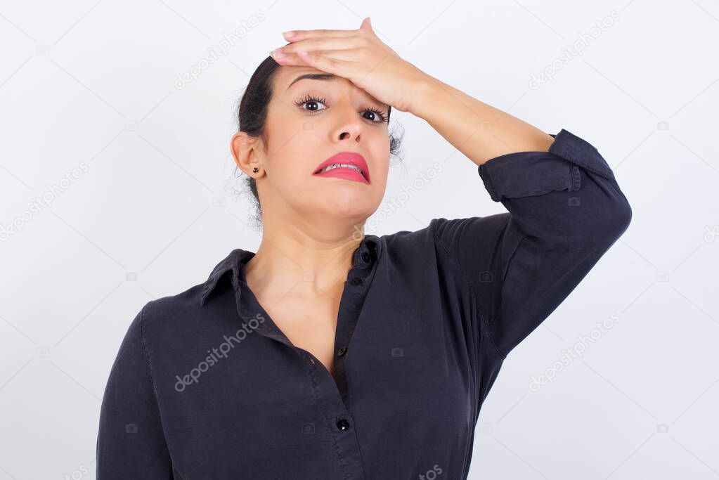 Oops, what did I do? Young beautiful Arab woman wearing gray dress against white studio background holding hand on forehead with frightened and regret expression.