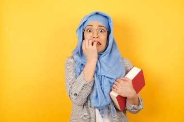 Endişe - güzel bir müslüman kadının kavramsal görüntüsü tesettüre sarılmış bir kitap ile ağzını eliyle kapatıyor ve boş bir arkaplana karşı duruyor. Bir şeyden ya da birinin çivi yemesinden korktun mu?.