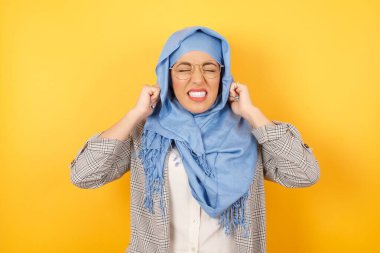 Bu sinir bozucu sesi çıkarmayı kes! Mutsuz, gergin, tesettürlü, tesettürlü, tesettürlü, kulaklarını parmaklarıyla tıkayan, üst katındaki komşulardan gelen gürültüden rahatsız olan genç Müslüman kadın..