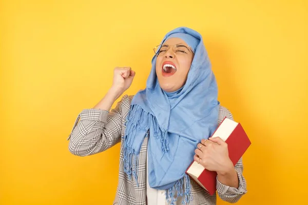 美しい若いイスラム教徒の女性は ヒジャーブの本を保持し 勝利のジェスチャーを表現することに興奮しています 成功し 勝利を祝う 優勝した スタジオの背景 — ストック写真