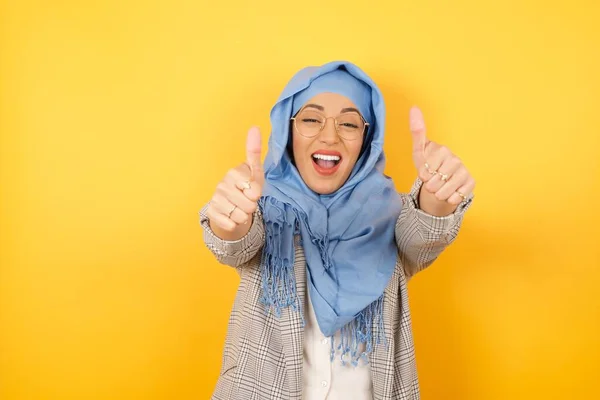 年轻的穆斯林妇女头戴头巾盖住孤立的背景 赞成用手做积极的手势 微笑着竖起大拇指 为成功感到高兴 看着摄像机 得奖的手势 — 图库照片