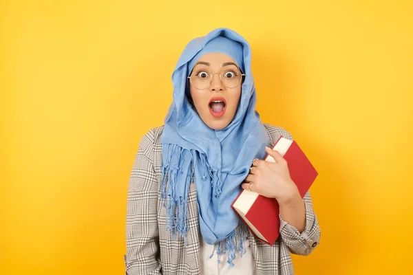 People and sudden reaction concept. Surprised young muslim woman wearing hijab, shrugs shoulders, looking sideways, being happy and excited about new plans with friends. Isolated over wall.