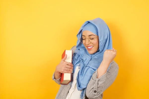Young muslim woman wearing hijab rejoicing her success and victory clenching her fists with joy. Lucky Arab woman being happy to achieve her aim and goals. Positive emotions, feelings.