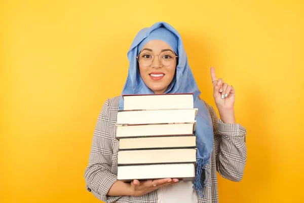 young muslim woman wearing hijab with books pointing up