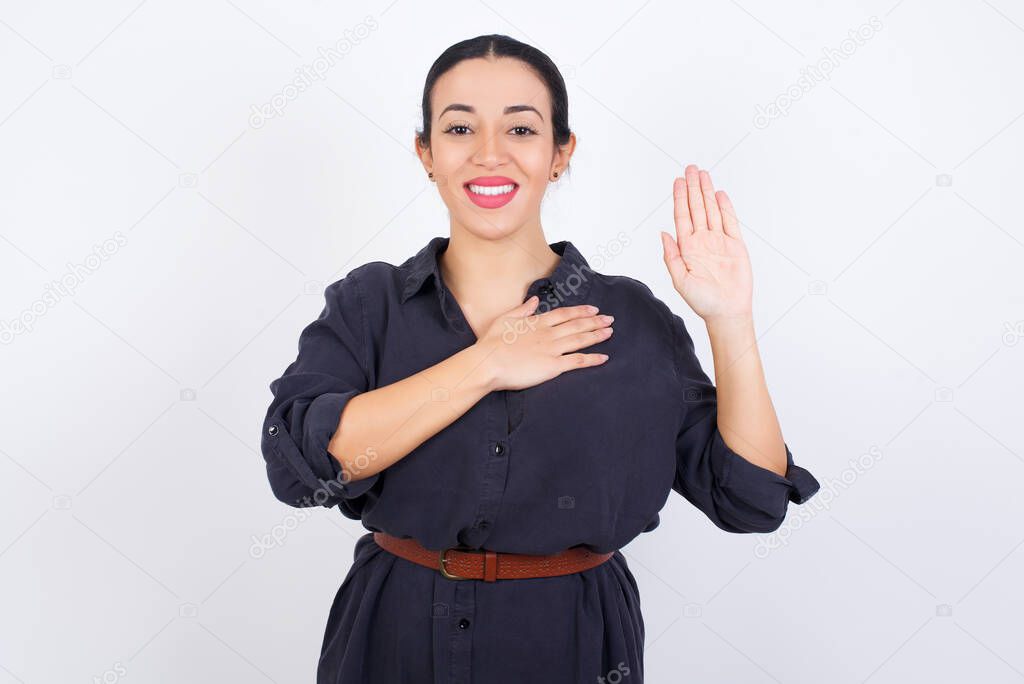 I swear, promise you not regret. Portrait of sincere  young beautiful latin woman wearing dress   raising one arm and hold hand on heart as give oath, telling truth, want you to believe.