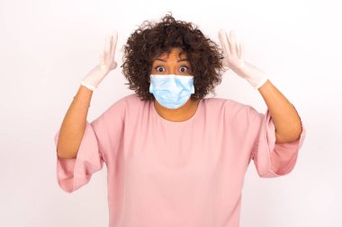 Yüzü maskeli genç bir kadın beyaz arka planda izole edilmiş. Bulaşıcı hastalıklara karşı koruma. Stüdyoda poz veren günlük kıyafetler giyen genç bir kadın.