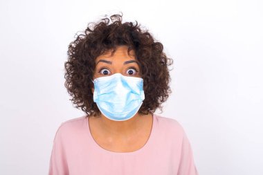 Maskeli genç bir kadın beyaz arka planda izole edilmiş. Bulaşıcı hastalıklara karşı koruma. Stüdyoda poz veren günlük kıyafetler giyen genç bir kadın.