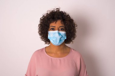 Maskeli genç bir kadın beyaz arka planda izole edilmiş. Bulaşıcı hastalıklara karşı koruma. Stüdyoda poz veren günlük kıyafetler giyen genç bir kadın.