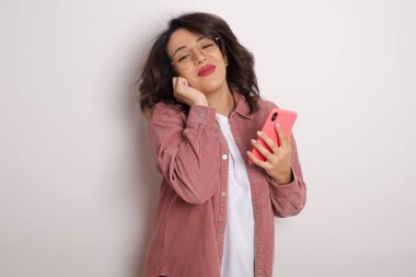 Stüdyoda gülümseyen akıllı telefonlu pembe tişörtlü güzel Latin bir kadın.