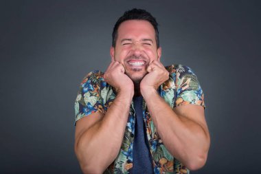 Yakışıklı beyaz adamın portresi duygularla dolup taşıyor, heyecanını ve mutluluğunu kapalı gözlerle ve ellerle ifade ederken gri arka planda geniş bir gülümsemeyle..