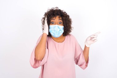 Yüz maskeli genç kadın beyaz arka planda izole edilmesine şaşırdı. Bulaşıcı hastalıklara karşı koruma. Gündelik kıyafetler giymiş genç bir kadın.