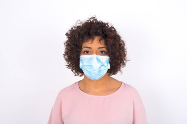 Maskeli genç bir kadın beyaz arka planda izole edilmiş. Bulaşıcı hastalıklara karşı koruma. Stüdyoda poz veren günlük kıyafetler giyen genç bir kadın.