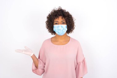 Yüz maskeli kadın beyaz arka planda izole edilmiş bir şey gösteriyor. Günlük kıyafetler giymiş, yüz maskesi takan genç bir kadın. Bulaşıcı hastalıklara karşı koruma.