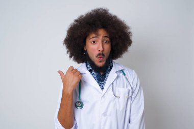 Tıbbi üniforma giyen, başparmağıyla işaret eden oldukça genç ve neşeli bir doktorun yatay görüntüsü gri arka planda izole edilmiş boş bir duvara işaret ediyor. Şuna bir bak..