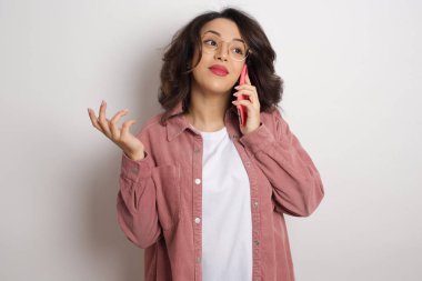 Stüdyoda akıllı telefondan konuşan genç ve güzel bir kadın. Beyaz duvara karşı cep telefonu tutan gözlüklü ve pembe ceketli bir Arap kadın.