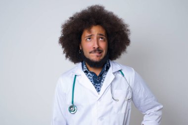 Tıp üniforması giyen doktor gergin ve korkmuş dudaklar ısırıyor sabırsız ifadeli kameraya bakıyor düşünceli, arka planda izole edilmiş tıbbi üniforma giyiyor..