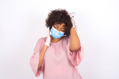 Beyaz arka planda, gözleri kapalı, maskeli genç bir kadın. Bulaşıcı hastalıklara karşı koruma. Gündelik kıyafetler giymiş genç bir kadın.