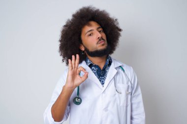 Tıbbi üniforma giyen doktorların onay olarak el işareti yapmalarına sevindim, iyimser bir ifadeye sahipler. Gri duvara yaslanarak.