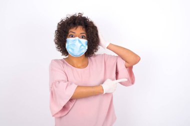 Yüzü maskeli genç bir kadın beyaz arka planda izole edilmiş. Bulaşıcı hastalıklara karşı koruma. Stüdyoda poz veren günlük kıyafetler giyen genç bir kadın.