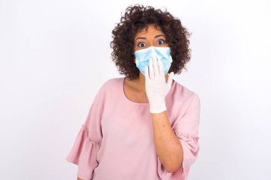 Maskeli genç bir kadın beyaz arka planda izole edilmiş. Günlük kıyafetler giymiş, yüz maskesi takan genç bir kadın. Bulaşıcı hastalıklara karşı koruma.