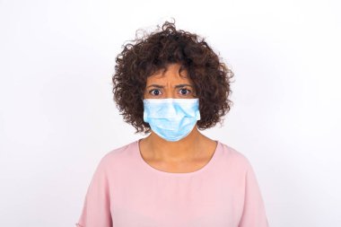 Yüzü maskeli genç bir kadın beyaz arka planda izole edilmiş. Bulaşıcı hastalıklara karşı koruma. Stüdyoda poz veren günlük kıyafetler giyen genç bir kadın.