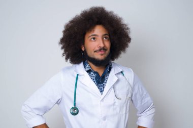 Beyaz önlüklü, neşeli genç bir doktorun yukarı bakıp bir şeyler düşündüğü belden yukarı pozlar. Ellerini kalçaya koy, yüz ifadenden şüphe et. Gri duvara yaslanmış bir şey olup olmadığını merak ediyorum..